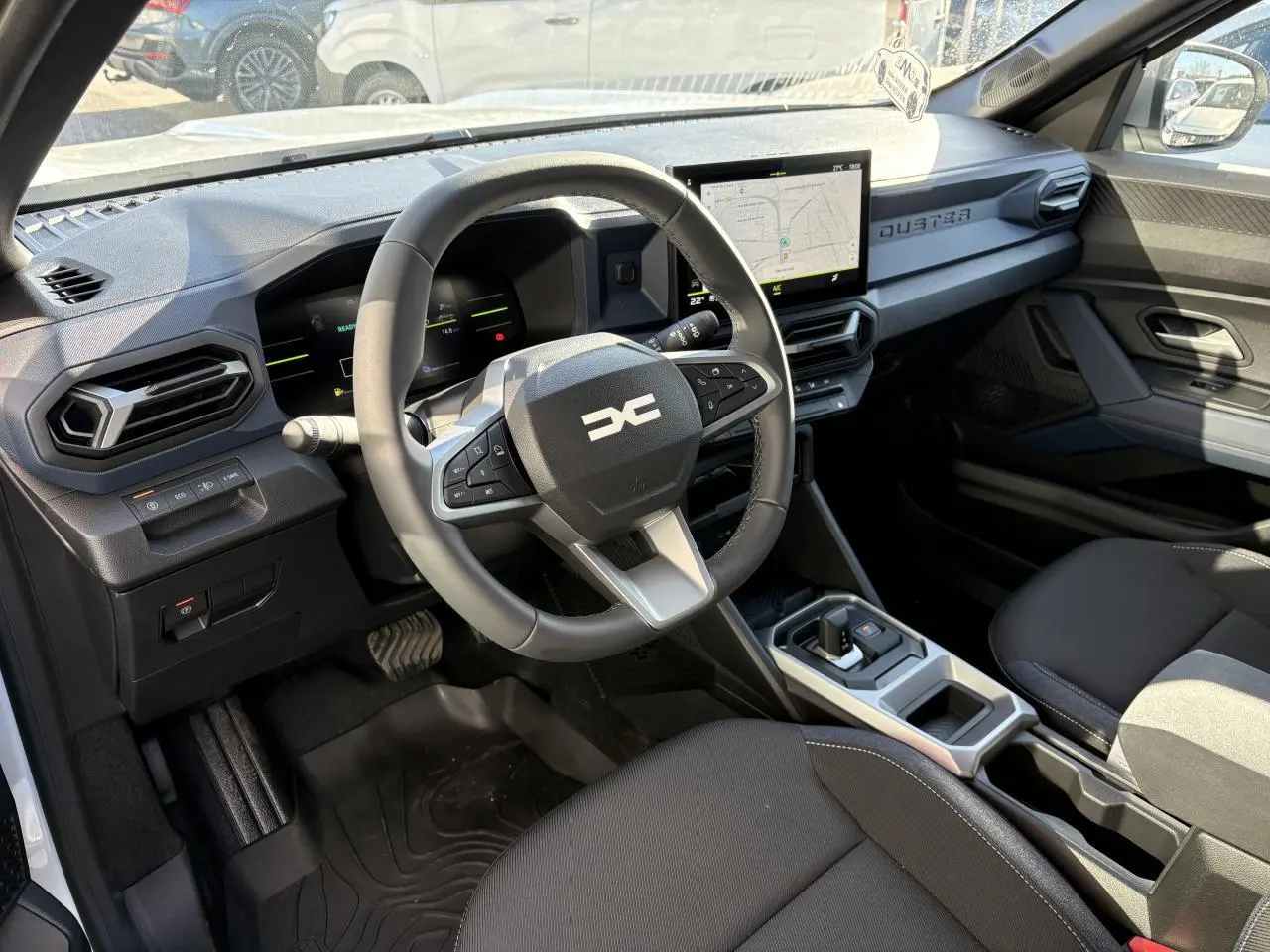 Vue intérieure côté conducteur du Dacia Duster 2024 blanc métallisé, avec tableau de bord digital et écran tactile central.
