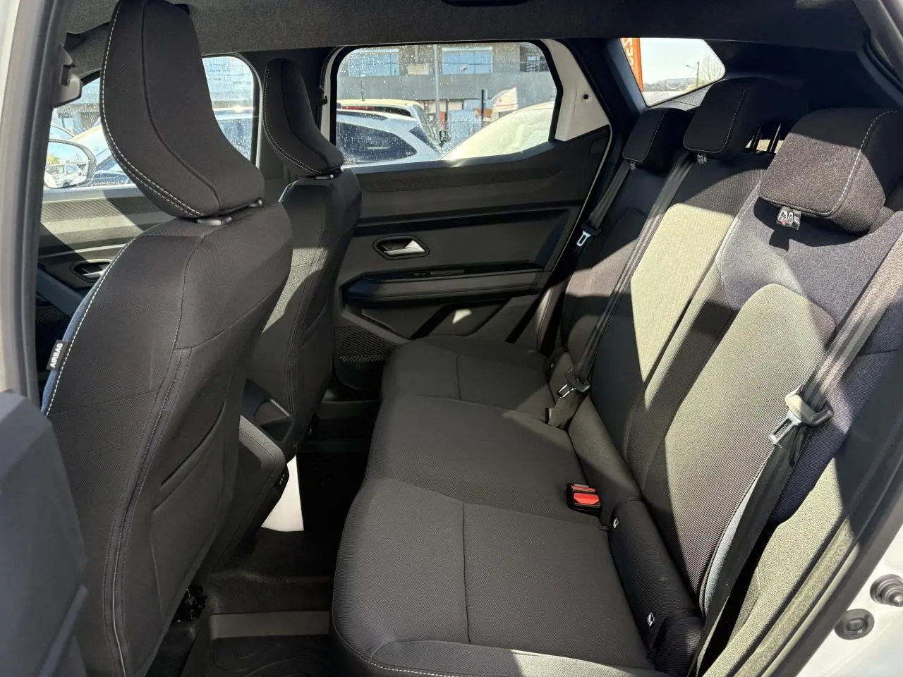 Vue intérieure côté droit sur la banquette arrière noire du Dacia Duster 1.6 Hybrid 2024 blanc métallisé.