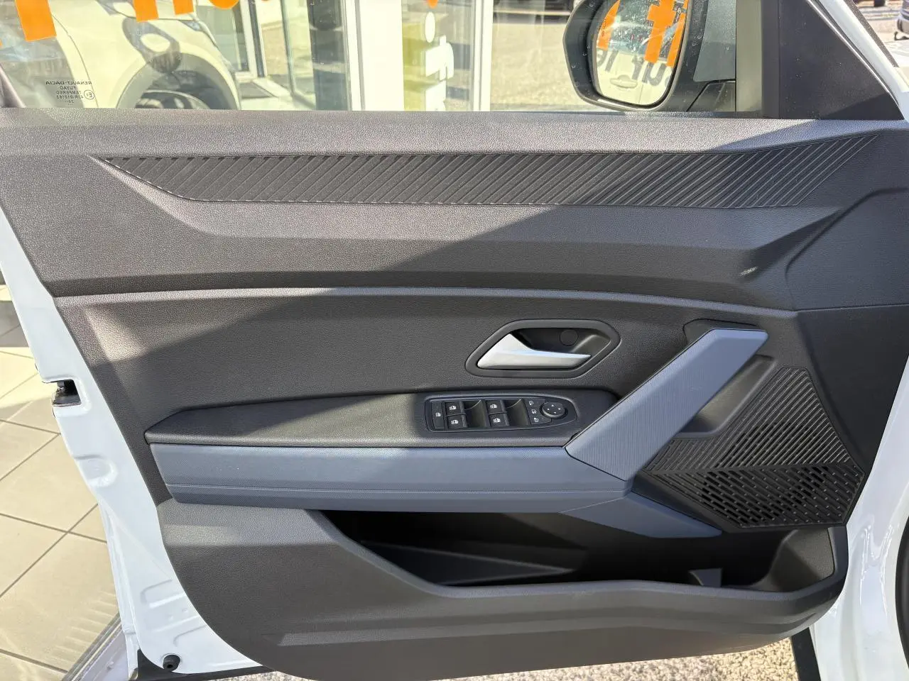 Vue rapprochée de la porte avant gauche blanche du Dacia Duster 2024 avec commandes électriques et accoudoir gris Denim.