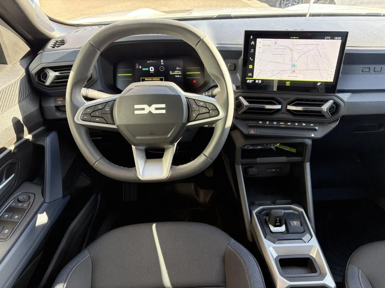Vue intérieure du tableau de bord et volant du Dacia Duster 1.6 Hybrid 2024 avec écran tactile et sellerie Denim.