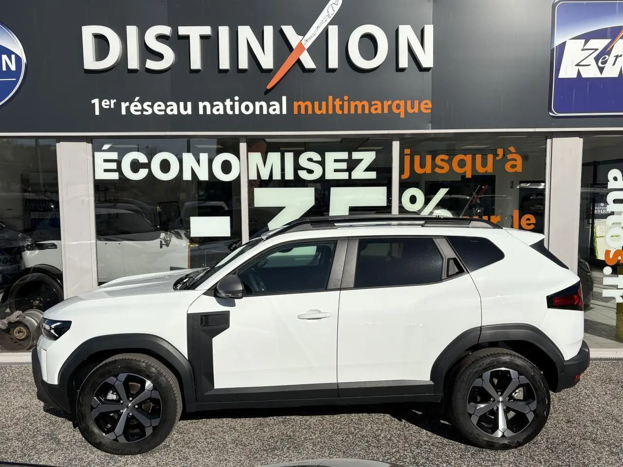 Profil côté gauche du Dacia Duster 2024 blanc métallisé avec barres de toit noires et jantes alliage 18 pouces.