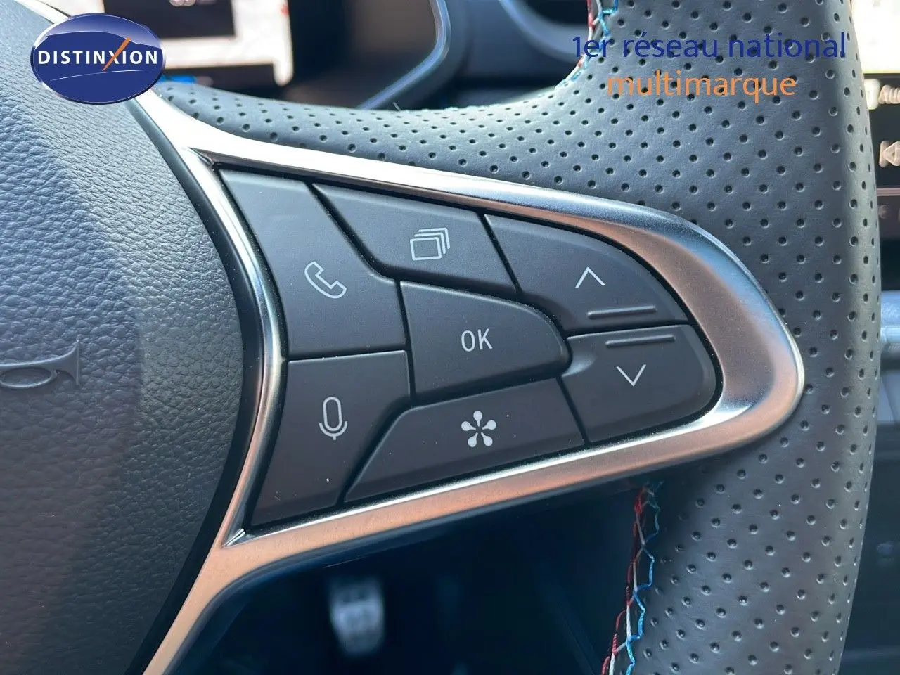 Gros plan sur les commandes multifonctions du volant perforé d'une Renault Captur E-Tech hybride bleu iron métal toit noir.