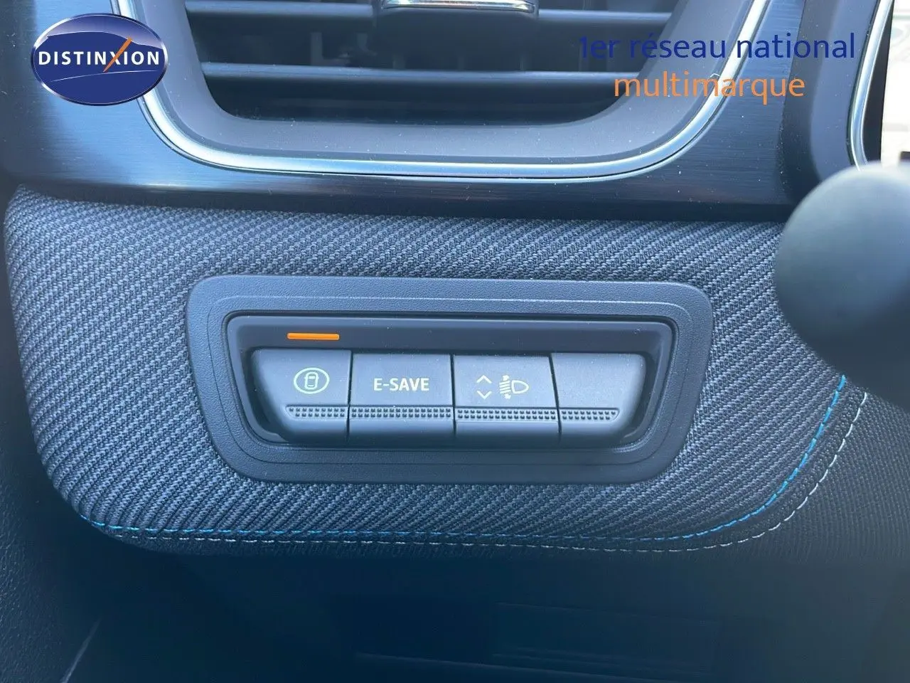 Gros plan sur les commandes E-SAVE et réglage des phares sur tableau de bord tissu bleu du Renault Captur hybride 2025.