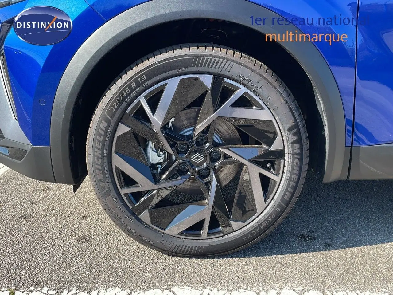 Gros plan sur la roue avant gauche du Renault Captur bleu Iron Metal avec jante noire au design géométrique.