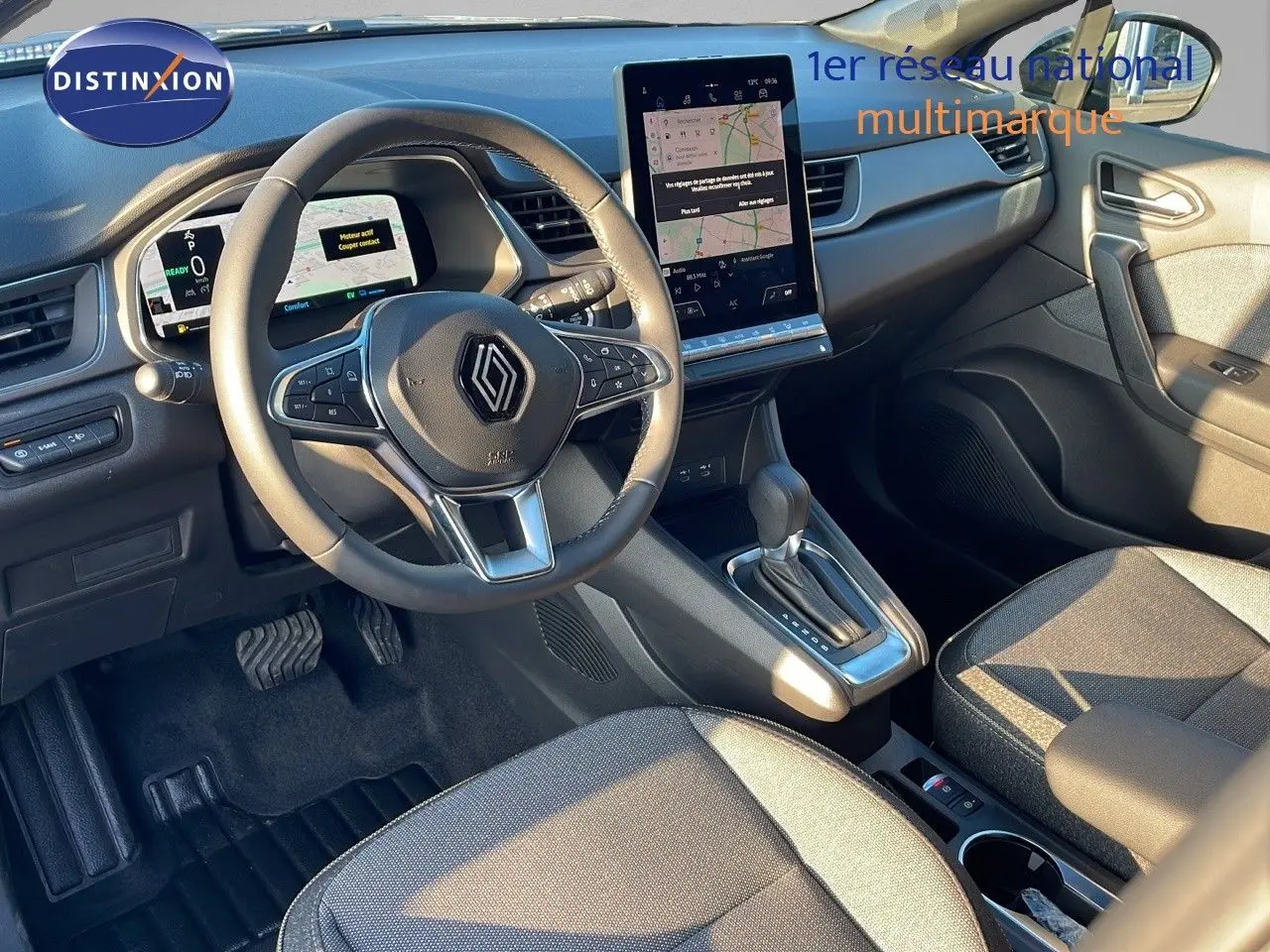 Vue intérieure du tableau de bord et volant de la Renault Captur E-Tech hybride, avec écran tactile central et sièges tissu noir-gris.