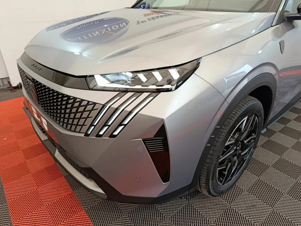 Vue 3/4 avant droit du Peugeot 3008 gris clair avec phares LED et calandre au design géométrique marqué.
