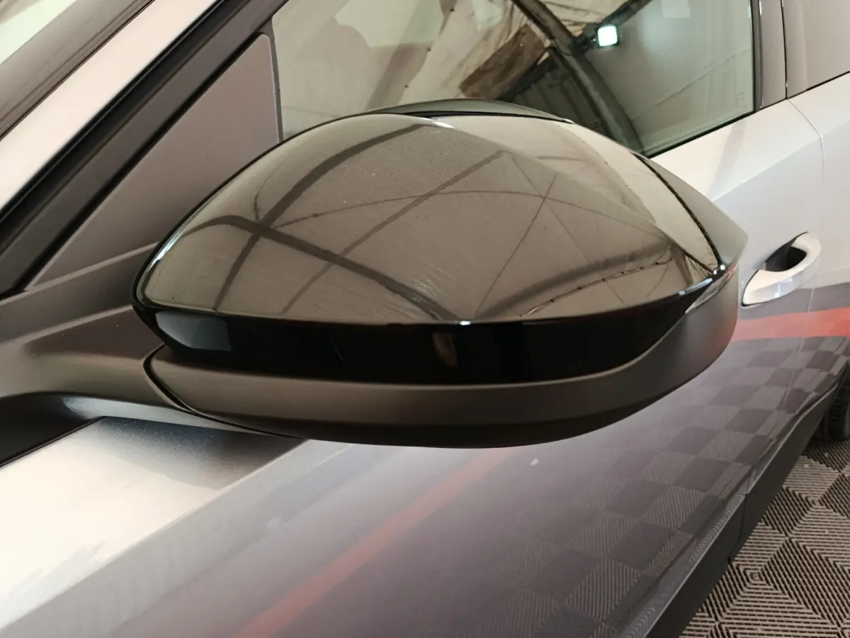 Rétroviseur noir en gros plan côté gauche sur Peugeot 3008 gris clair, avec reflet de la structure du plafond.