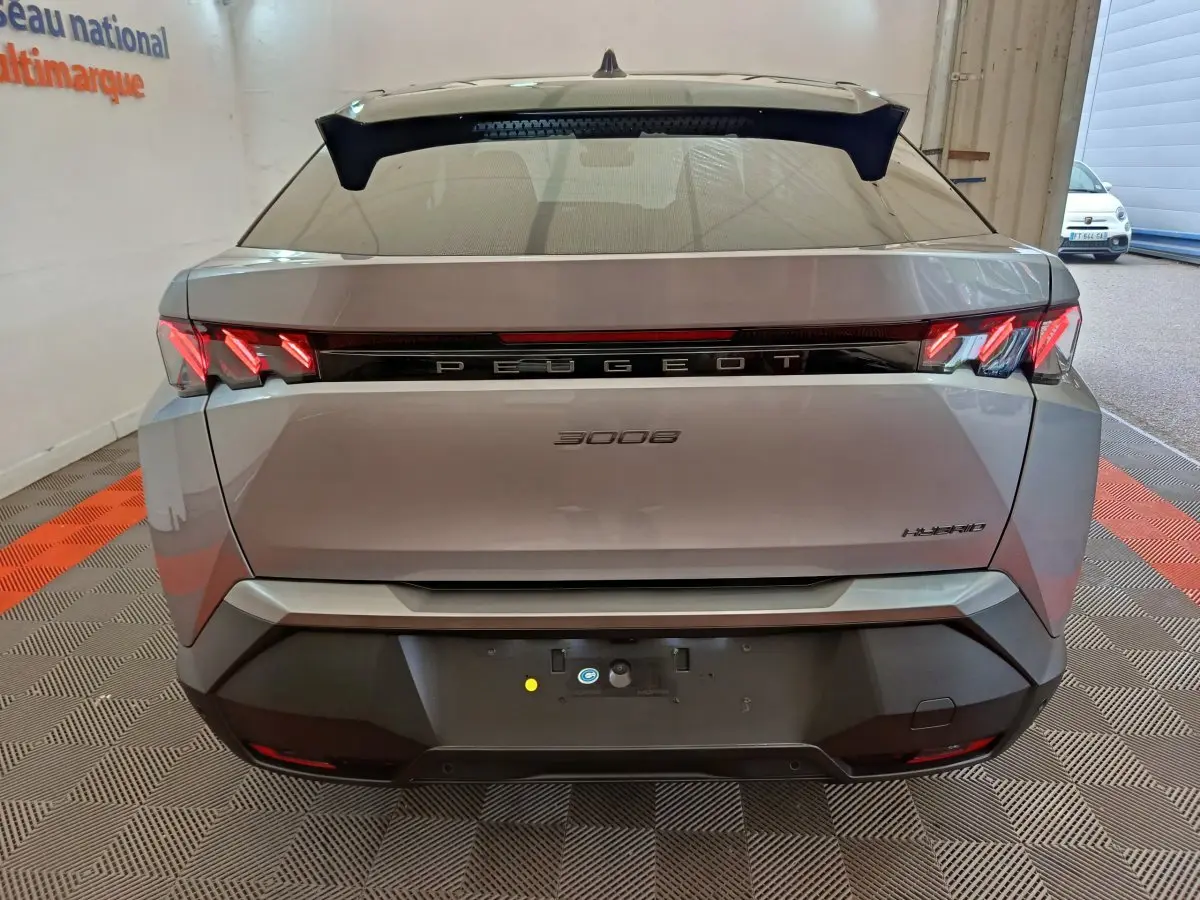 Vue arrière d’un Peugeot 3008 gris clair hybride 2025 avec feux LED et logo lumineux central sur fond noir.