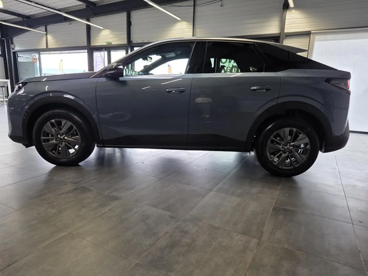 Vue latérale droite du Peugeot 3008 hybride bleu Obsession avec jantes alliage 18 pouces et toit noir en intérieur showroom.