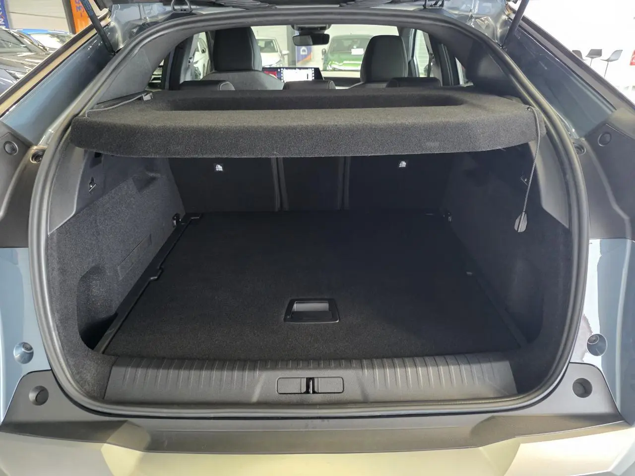 Coffre ouvert vu de l'arrière d'un Peugeot 3008 bleu hybride 2026, avec cache-bagages et intérieur noir.