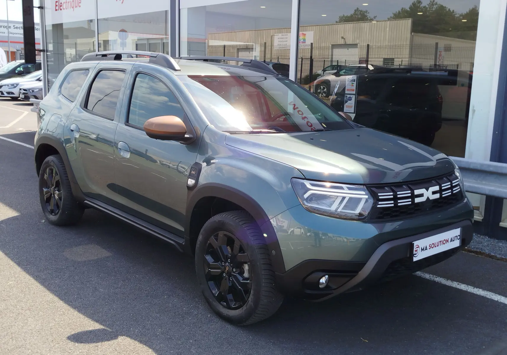 Dacia Duster 2024 vert cèdre métallisé en 3/4 avant droit, avec jantes noires et coques de rétroviseur bronze.