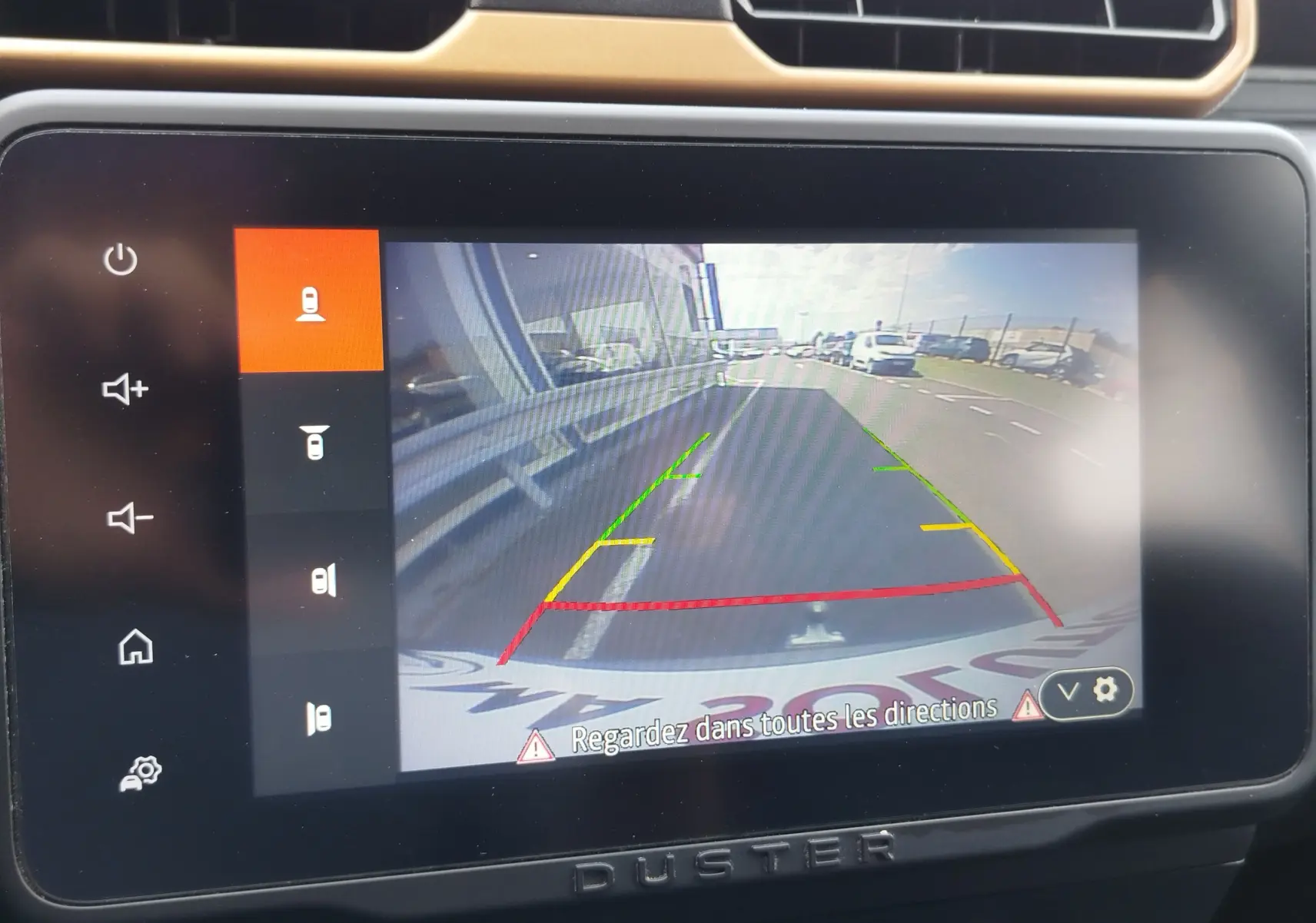 Écran de caméra de recul du Dacia Duster 2024, vue arrière avec lignes de guidage colorées sur route asphaltée.