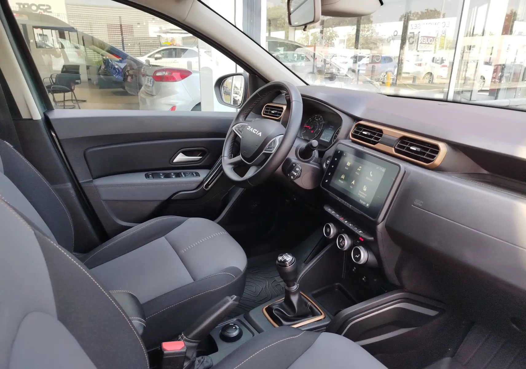 Vue intérieure côté conducteur du Dacia Duster 2024, montrant le volant, la console centrale avec écran tactile et levier de vitesses manuel.