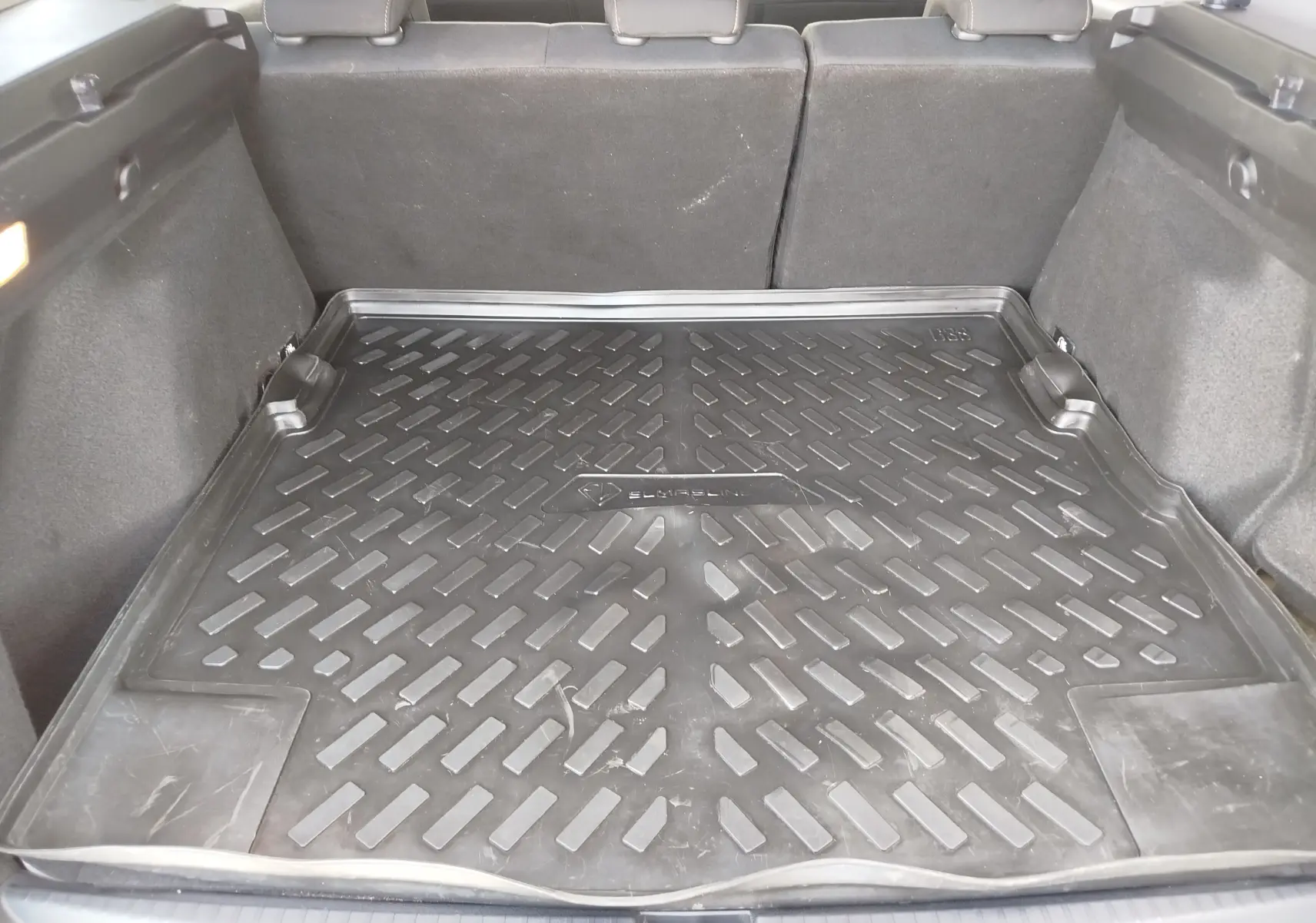 Coffre ouvert vu de l'arrière d'un Dacia Duster 2024, avec tapis de protection noir et sièges arrière rabattus.
