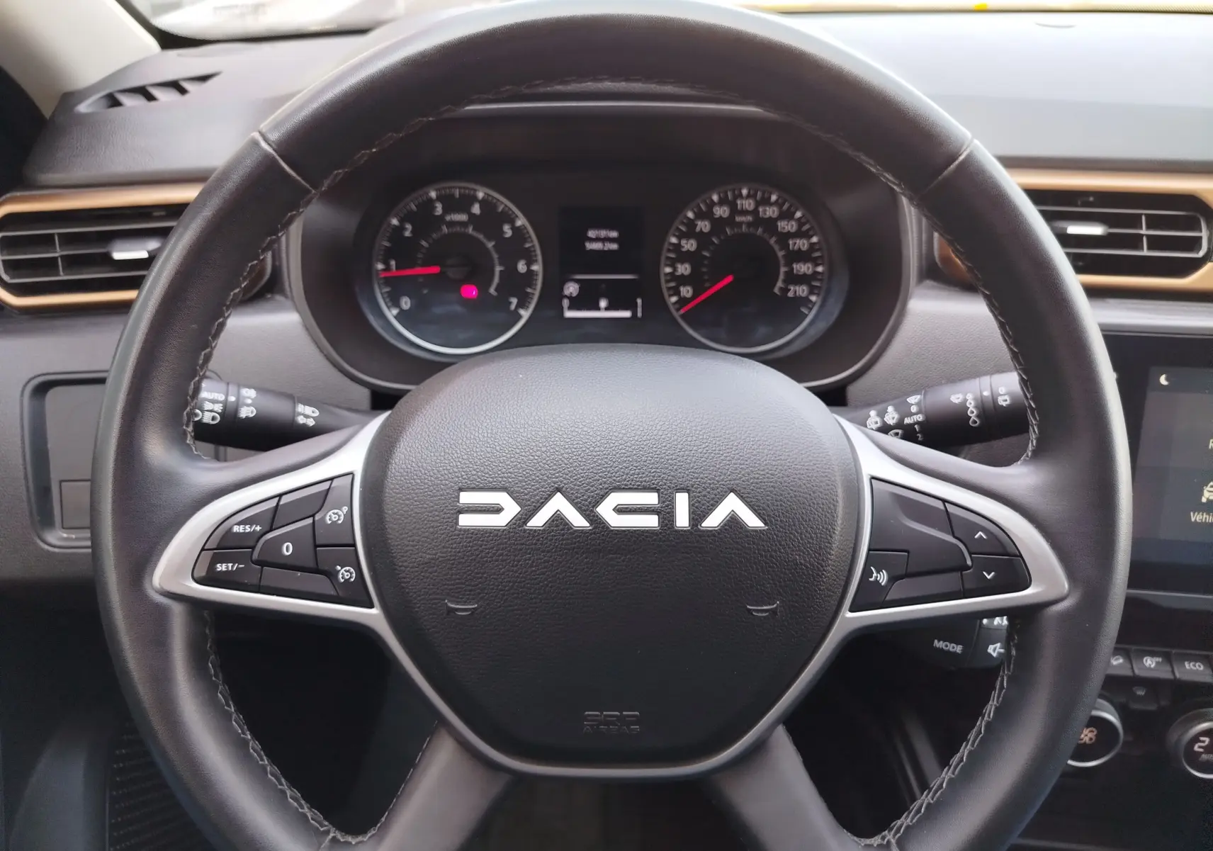 Vue rapprochée du volant noir du Dacia Duster 2024 avec commandes intégrées et tableau de bord en arrière-plan.
