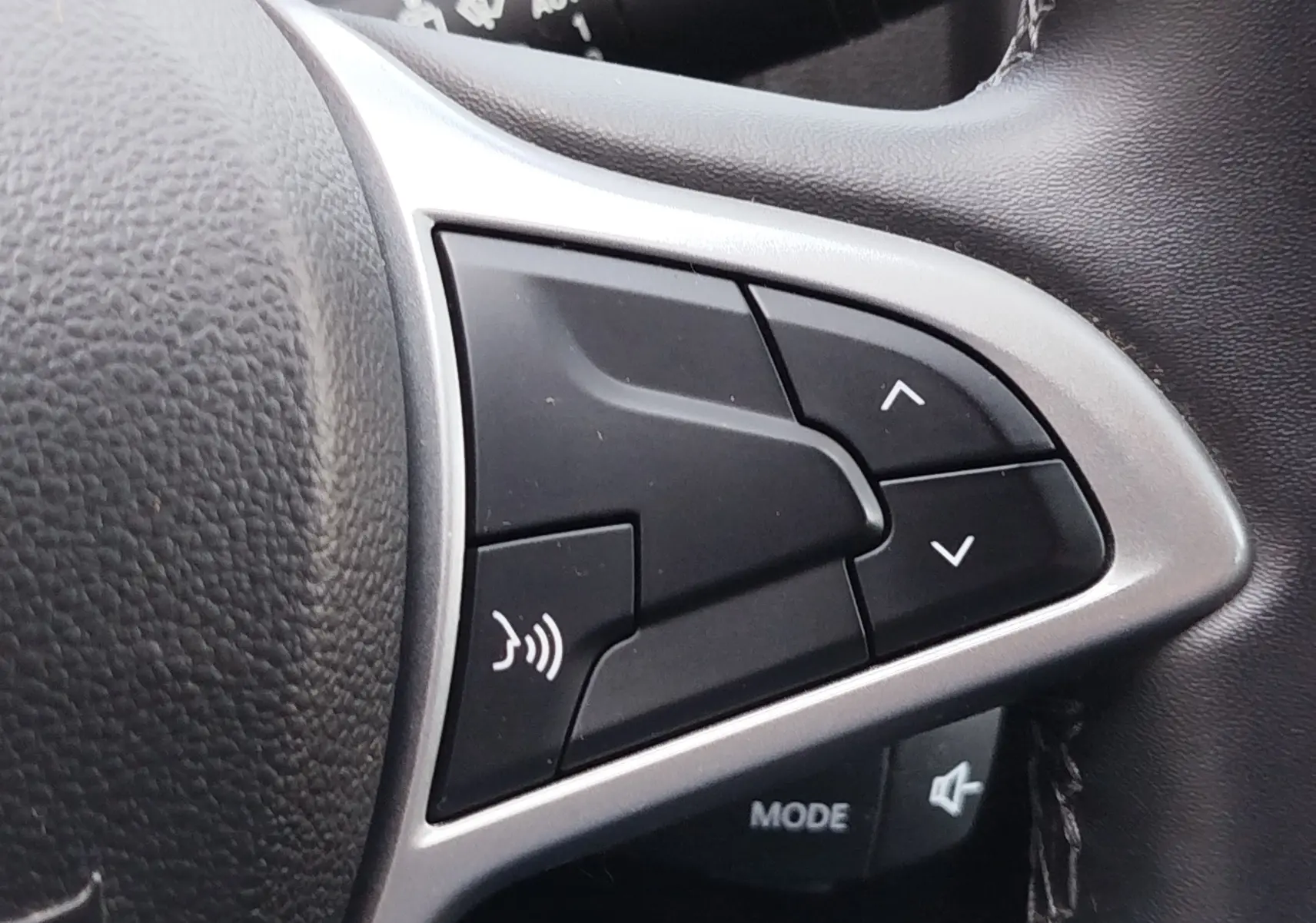 Gros plan sur les commandes au volant du Dacia Duster 2024, boutons noirs avec cadre argenté et cuir noir texturé.
