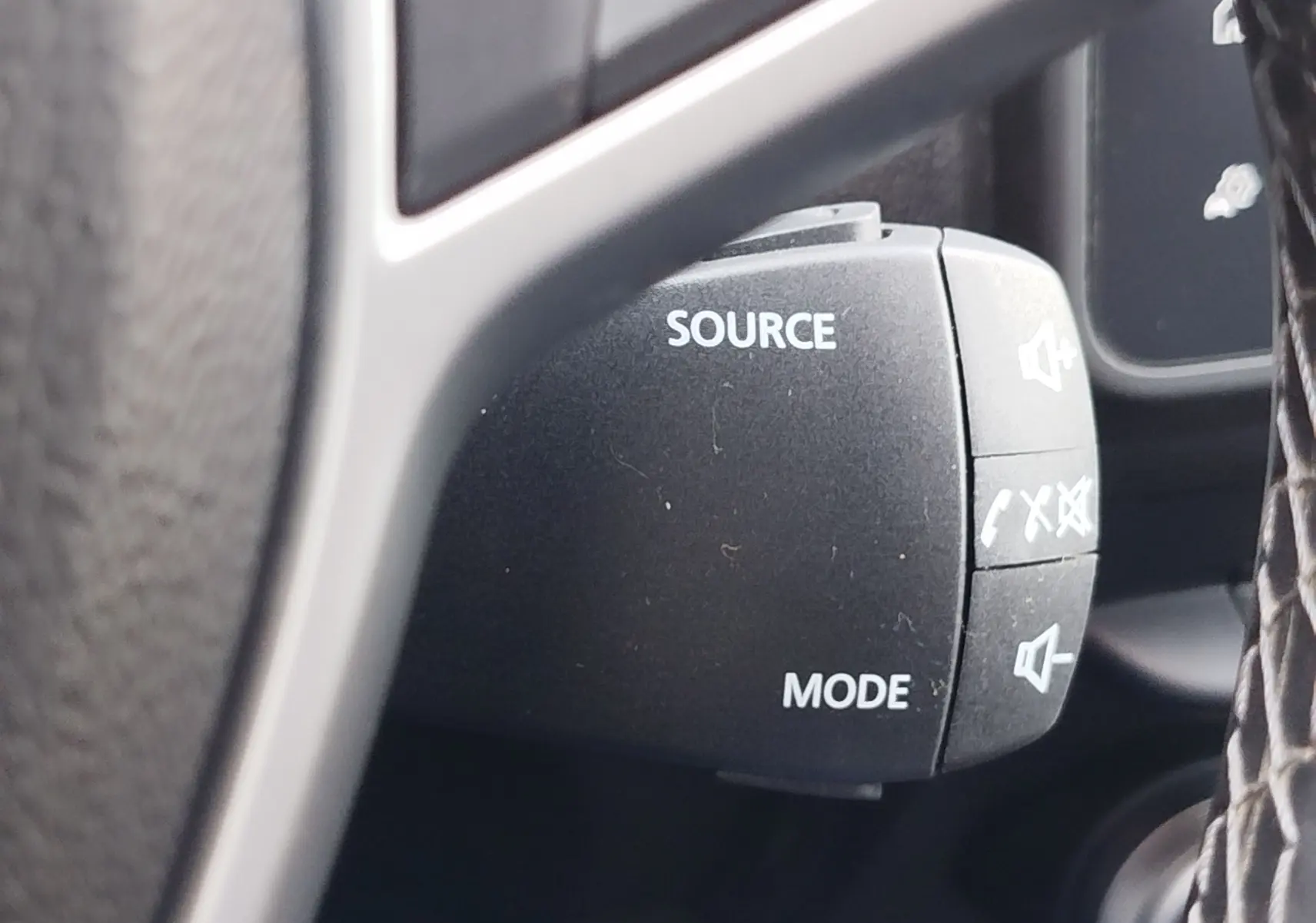 Détail du commodo audio avec boutons source et mode sur le volant d’un Dacia Duster 2024, intérieur noir.