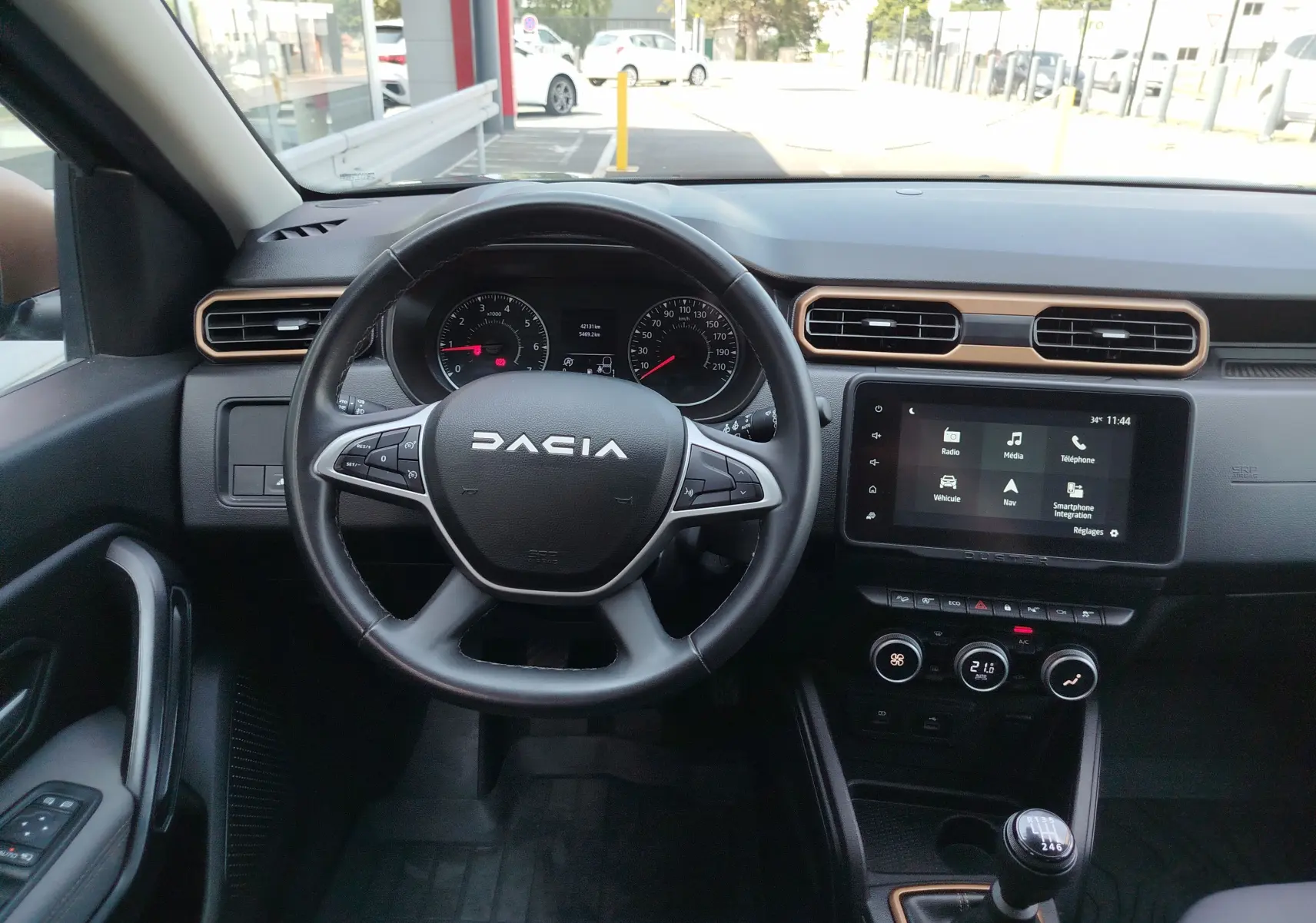 Vue intérieure du tableau de bord du Dacia Duster 2024, avec volant, écran tactile et levier de vitesses manuel.