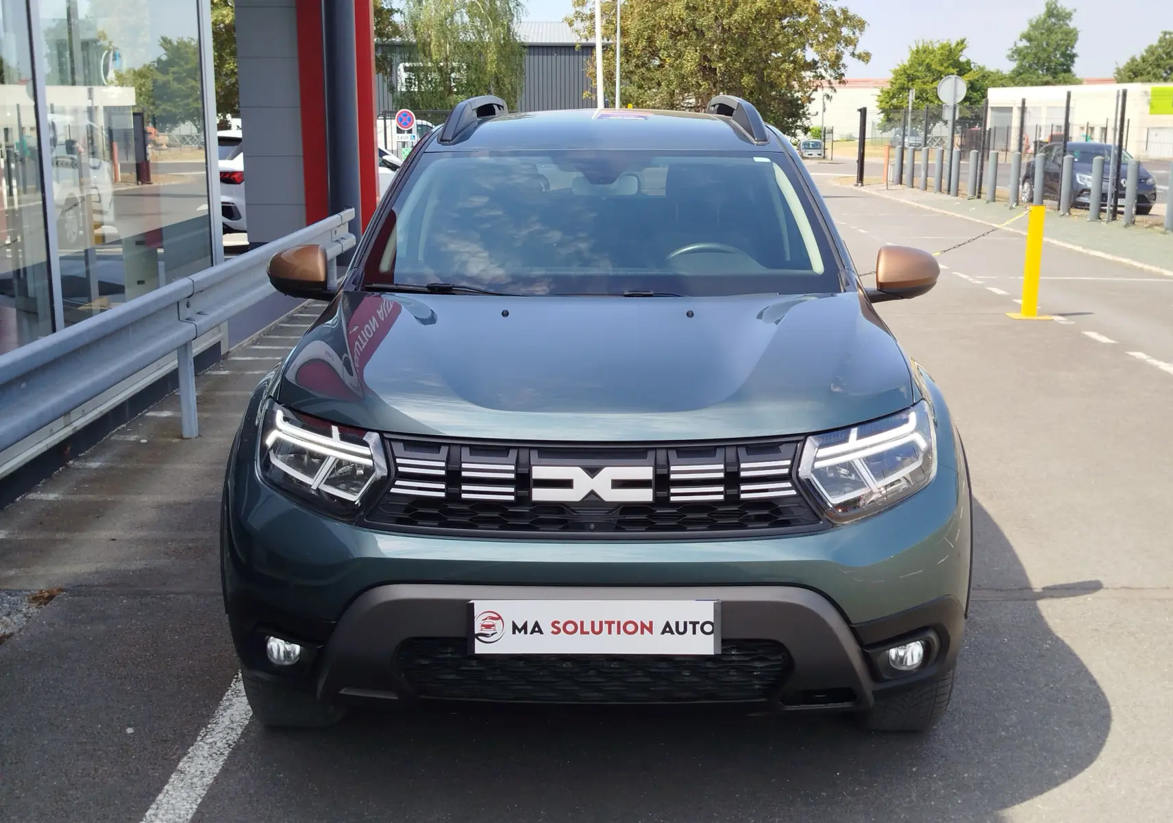 Vue avant d'un Dacia Duster 2024 vert cèdre métallisé avec calandre noire et feux LED allumés, stationné en extérieur.