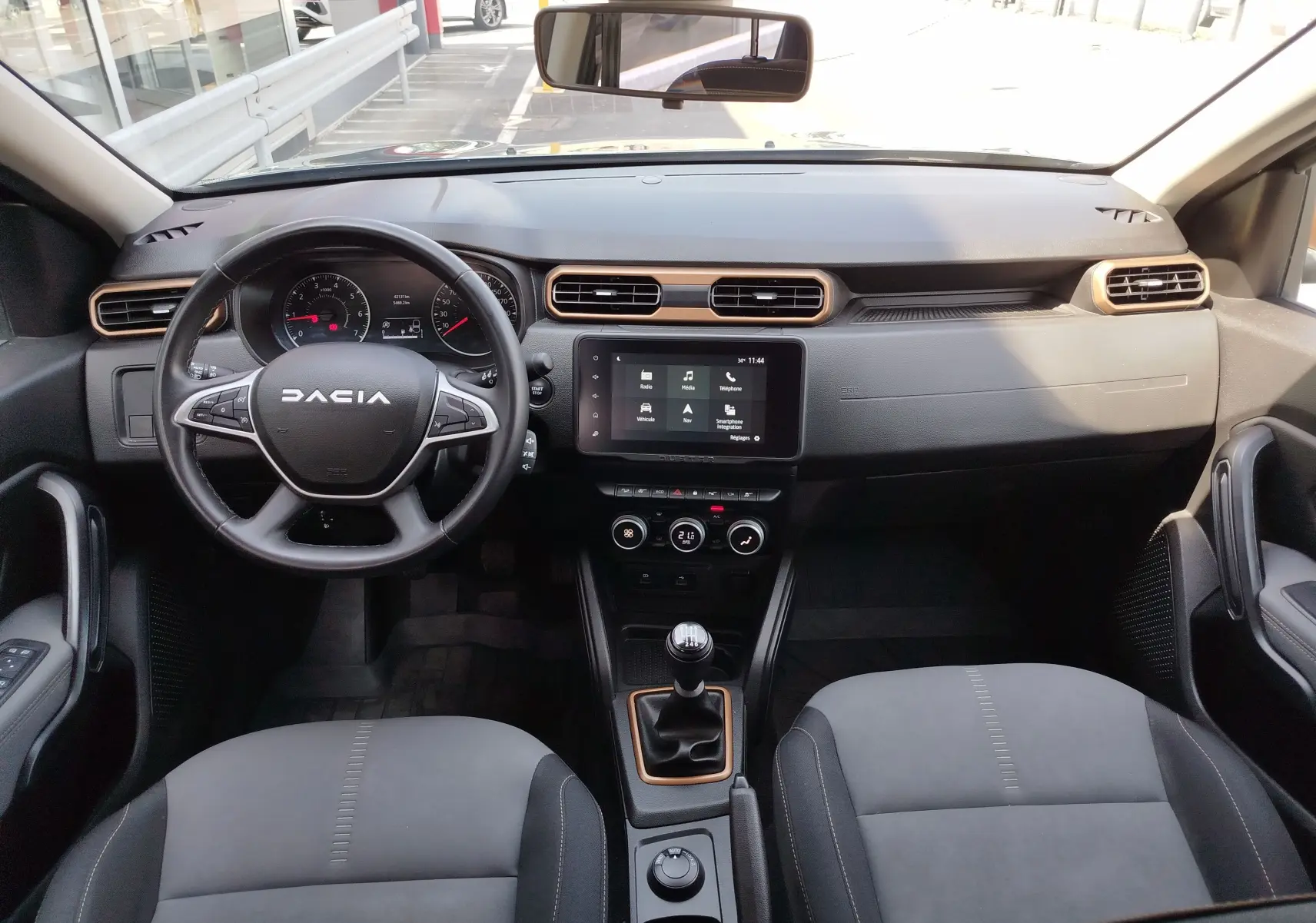 Vue intérieure frontale du Dacia Duster 2024, tableau de bord noir avec touches cuivrées et volant multifonction.