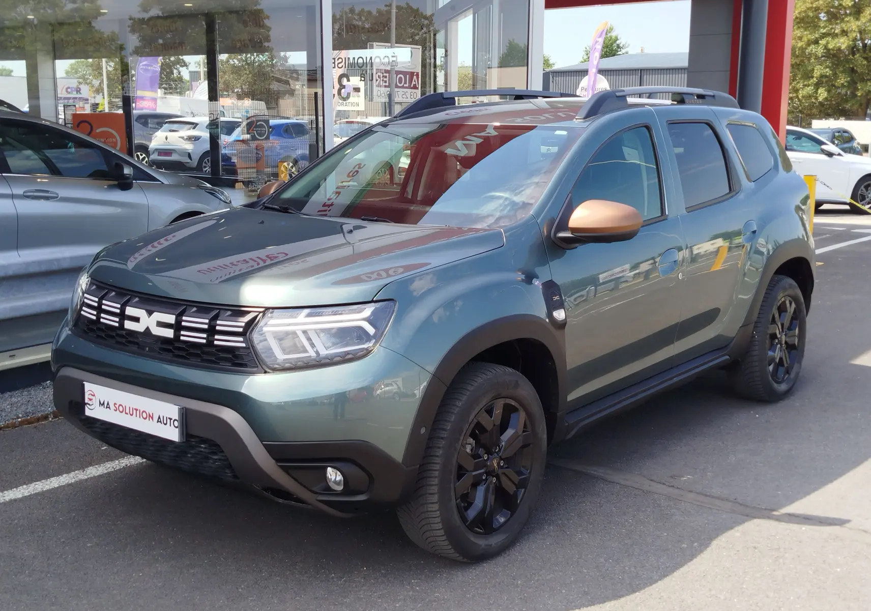 Dacia Duster 2024 vert cèdre métallisé en 3/4 avant droit avec jantes noires et coques de rétroviseurs bronze.