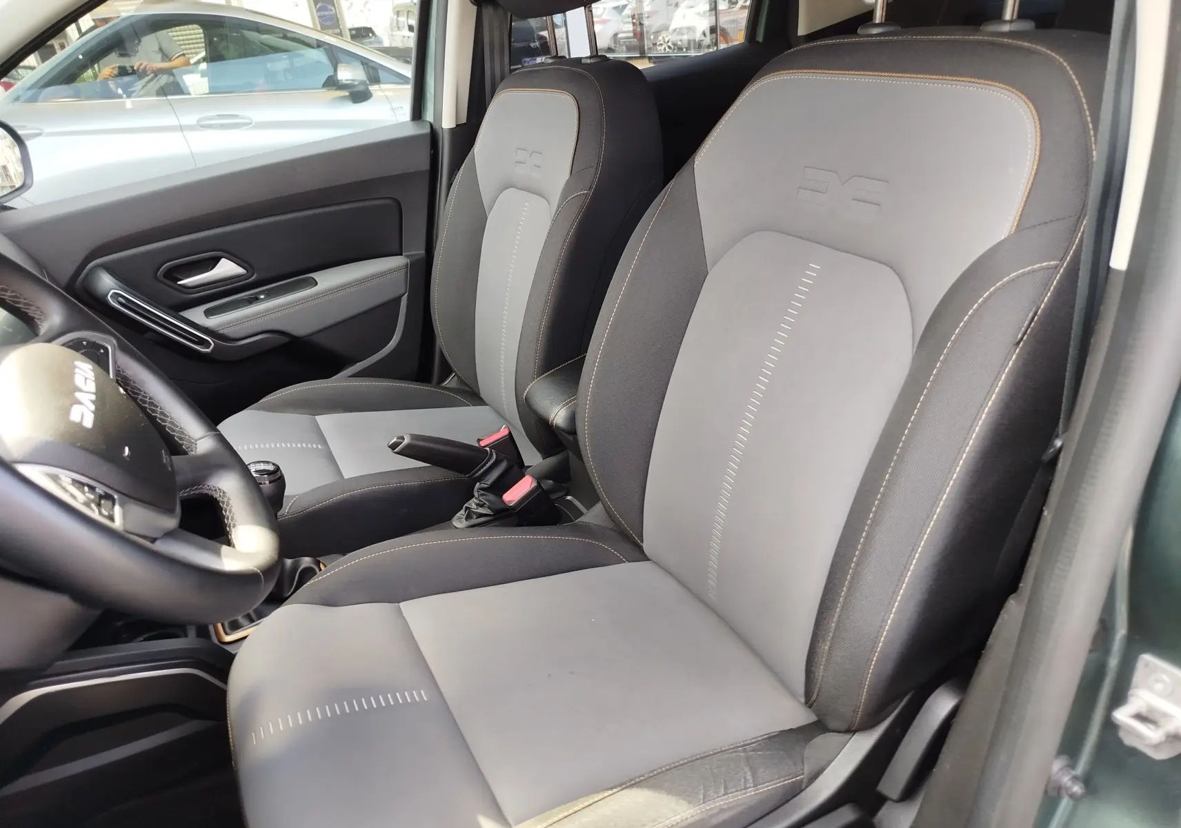 Intérieur du Dacia Duster 2024 vu côté conducteur, sièges bi-matière gris et noir avec surpiqûres orange.