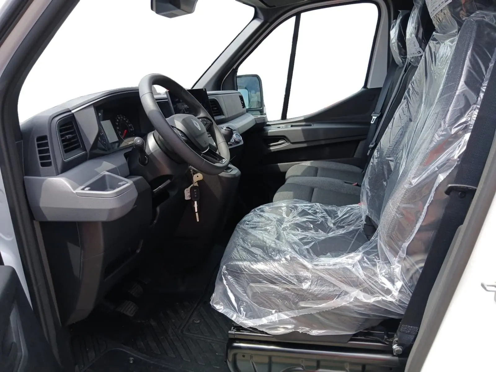 Vue intérieure côté conducteur du Renault Master blanc 2026, sièges protégés par film plastique, volant et tableau de bord visibles.