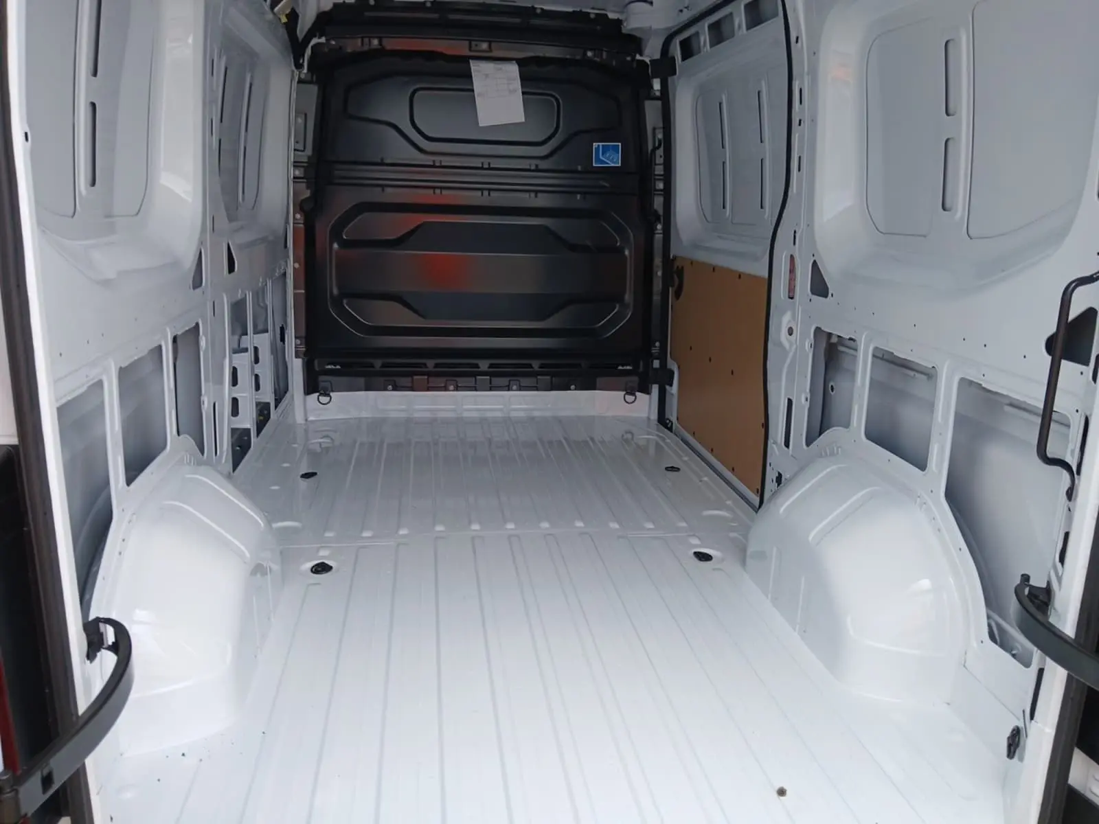 Vue intérieure arrière du Renault Master blanc L2H2, montrant l'espace de chargement vide avec cloison noire et paroi latérale partiellement protégée.