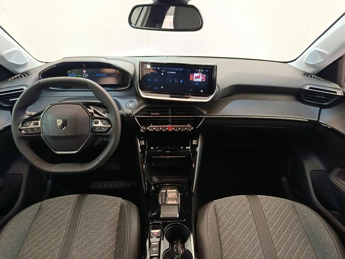 Intérieur de la Peugeot 208 électrique 2024 vu de face, tableau de bord noir avec écran tactile central et volant cuir.