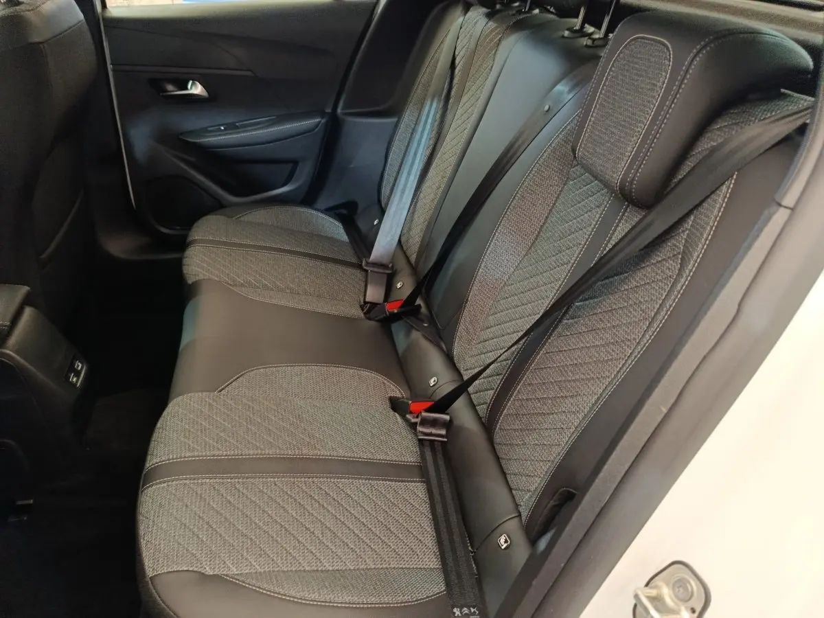 Vue côté droit sur la banquette arrière grise et noire du Peugeot 208 électrique blanc 2024, avec ceintures attachées.