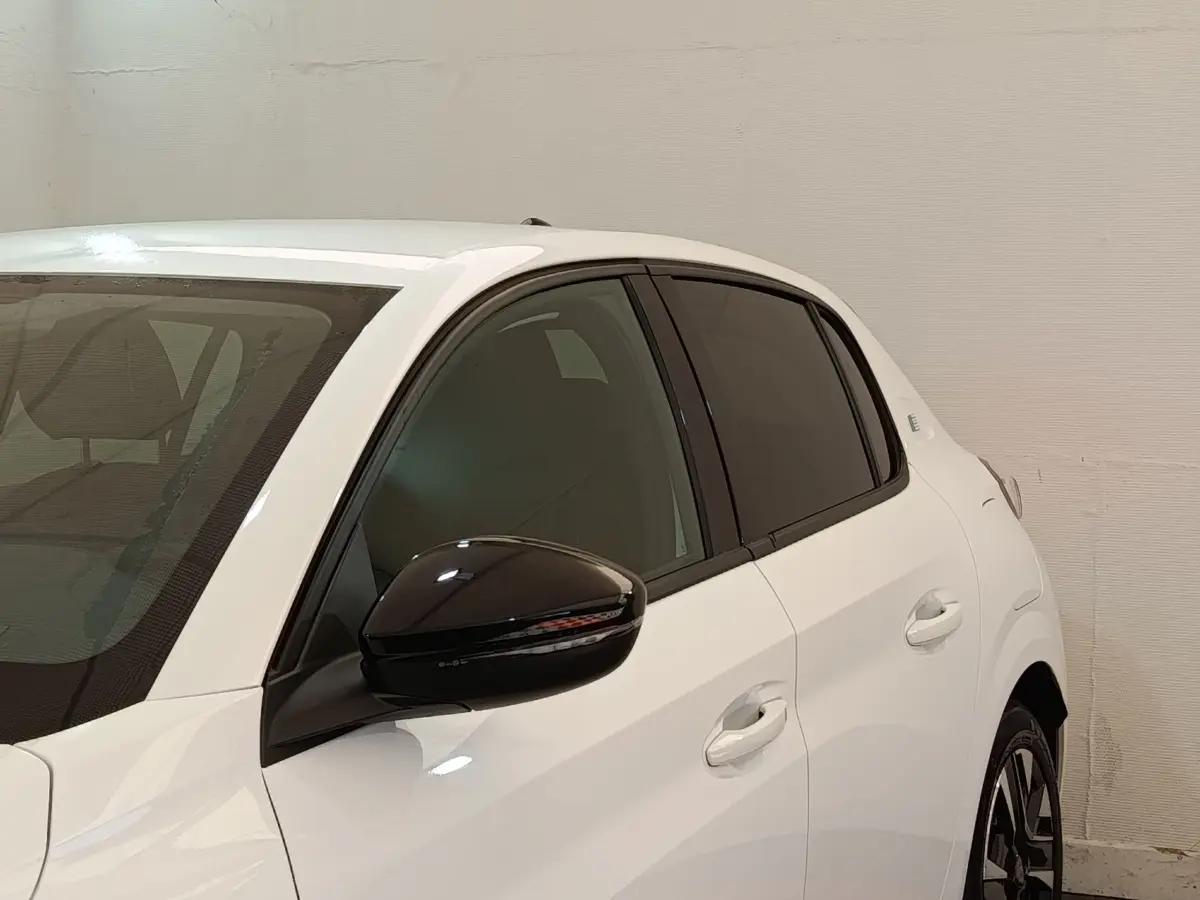 Vue latérale droite d'une Peugeot 208 électrique blanche avec rétroviseur noir et vitres teintées.
