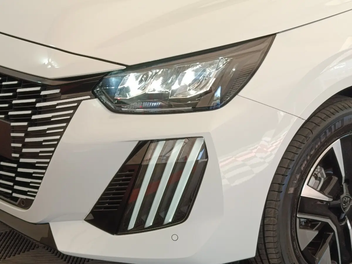 Gros plan avant droit du Peugeot 208 électrique blanc 2024, mettant en valeur les phares LED et la calandre distinctive.