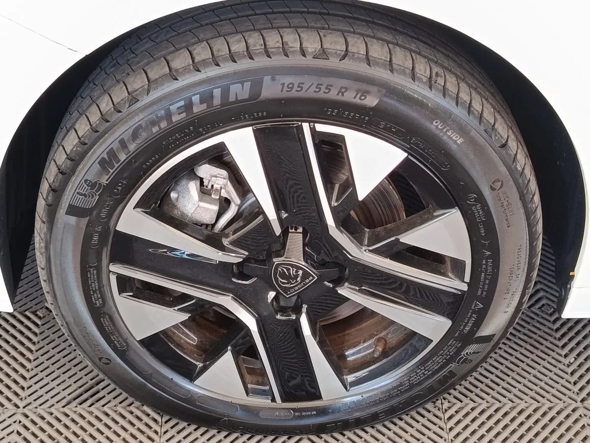 Gros plan sur la roue avant droite blanche d’une Peugeot 208 électrique 2024 avec jante alliage noire et argent.