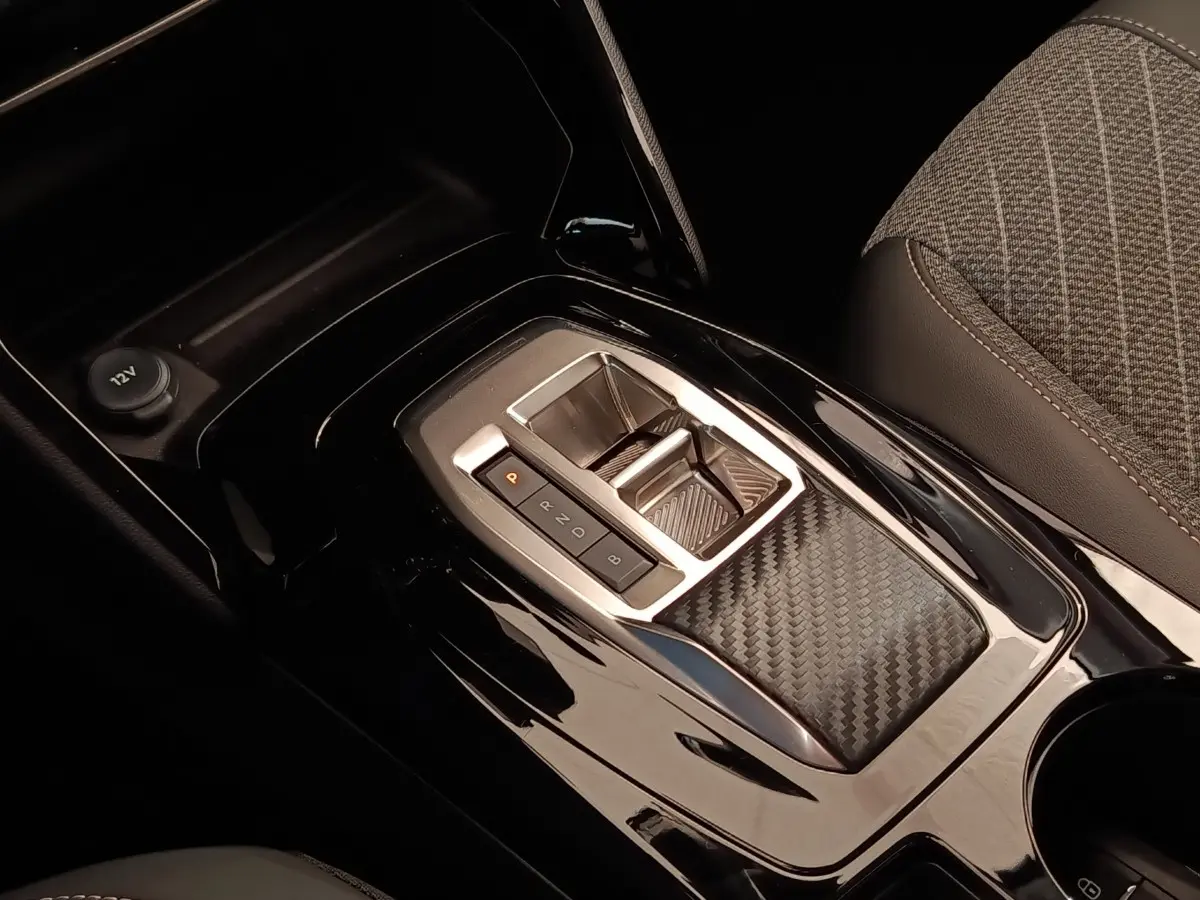 Gros plan sur la console centrale noire brillante avec sélecteur de vitesses et accoudoir tissu gris de la Peugeot 208 électrique.