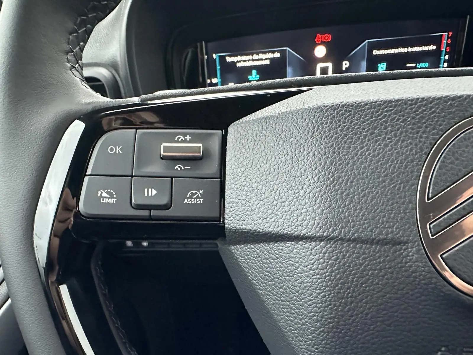 Gros plan sur les commandes gauche du volant du Citroën Berlingo 2025, avec affichage numérique en arrière-plan.