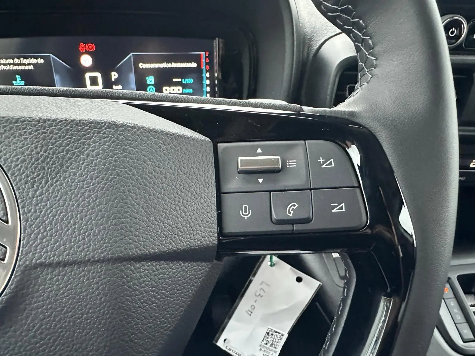 Gros plan sur les commandes au volant noir du Citroën Berlingo 2025, avec tableau de bord digital en arrière-plan.