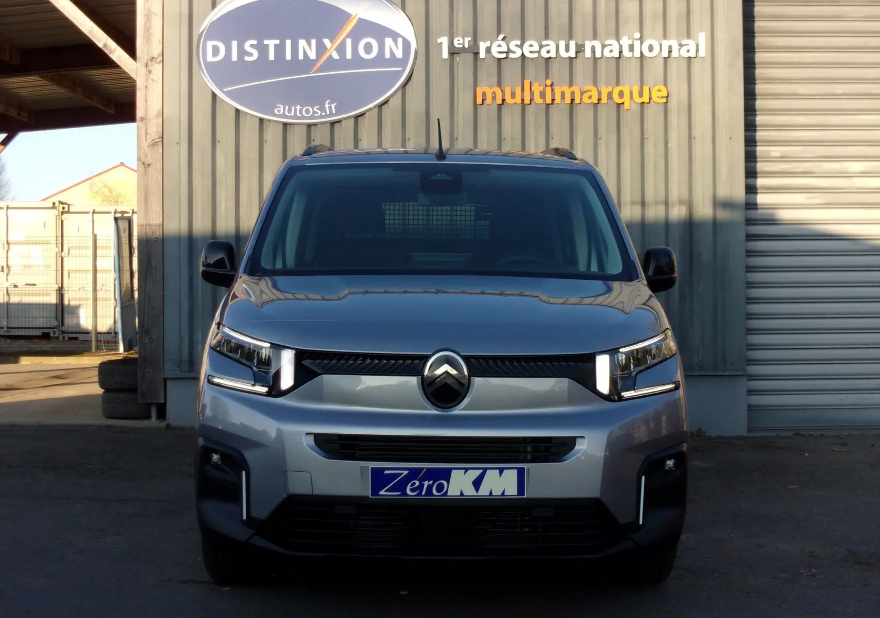 Vue frontale d'un Citroën Berlingo gris Artense 2025 avec phares LED et calandre moderne, devant un bâtiment industriel.