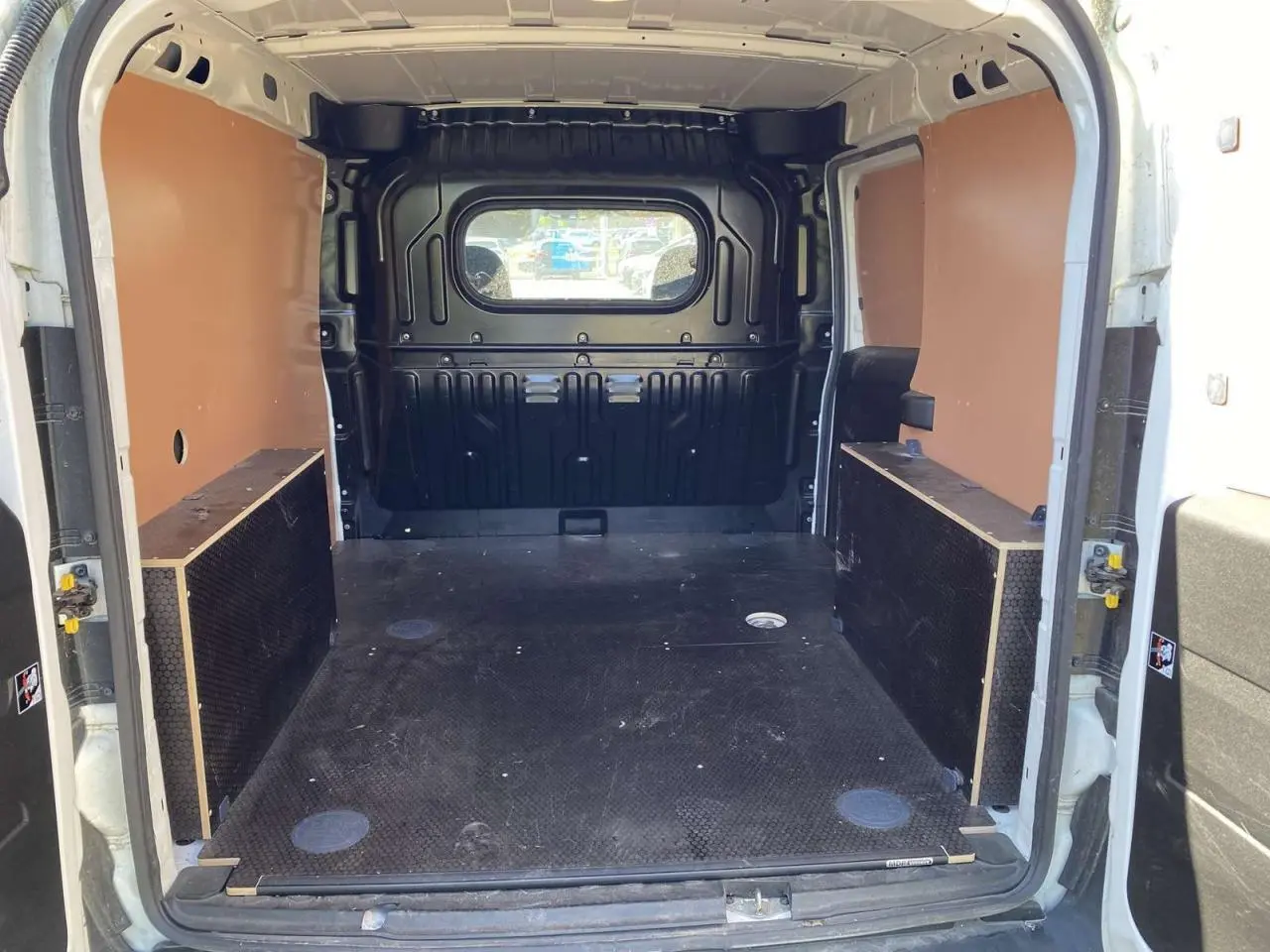Vue intérieure arrière du fourgon blanc FIAT Doblo 2017, montrant l'espace de chargement avec kit bois et paroi vitrée.