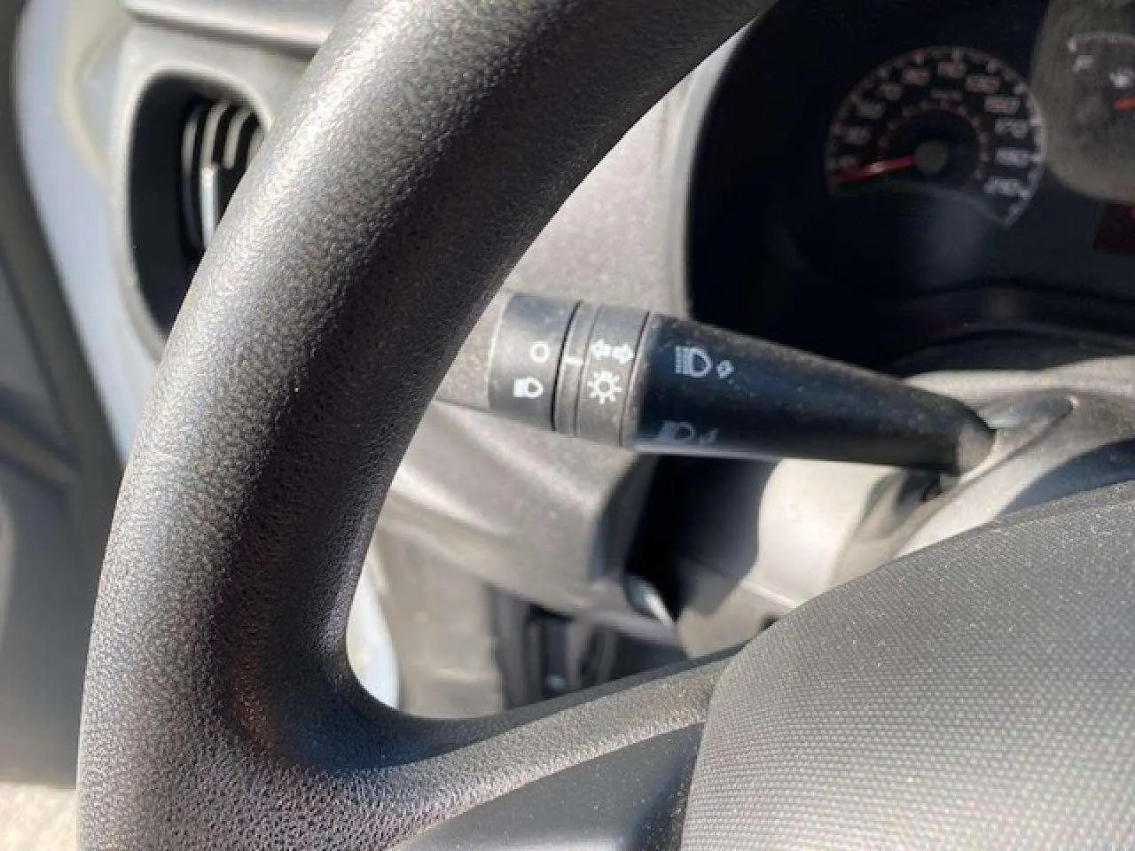 Gros plan sur le volant et la manette de clignotant du Fiat Doblo blanc, montrant le tableau de bord partiellement visible.