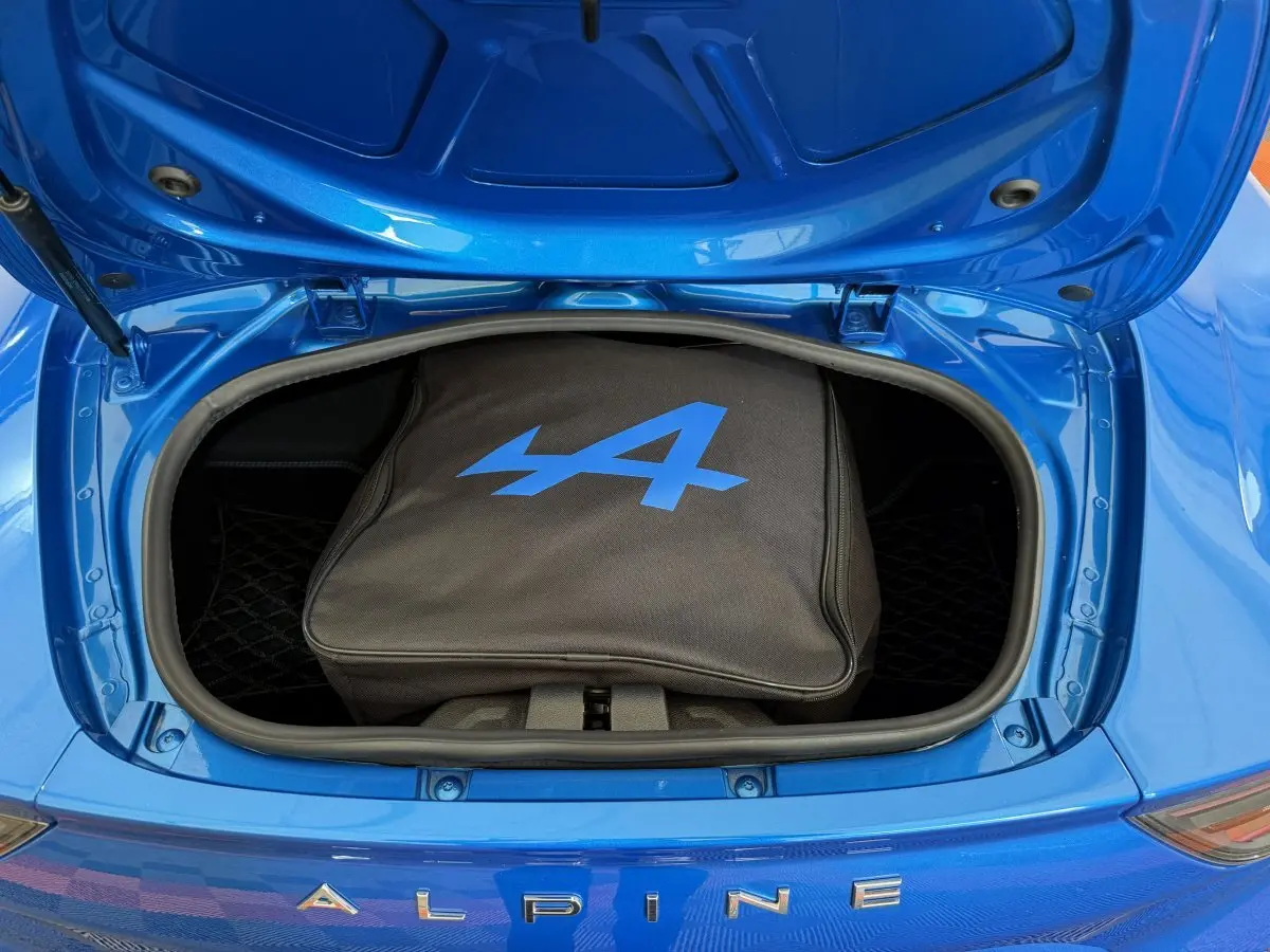 Vue plongeante sur le coffre avant ouvert d'une Alpine A110 Legende bleue avec sac de rangement noir marqué du logo bleu.