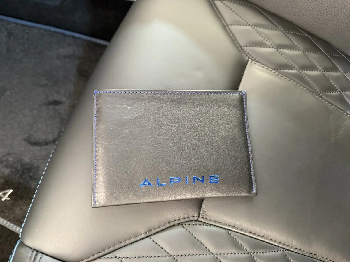 Gros plan sur une pochette Alpine noire avec coutures bleues posée sur un siège en cuir noir matelassé de l'Alpine A110 Legende 2019.