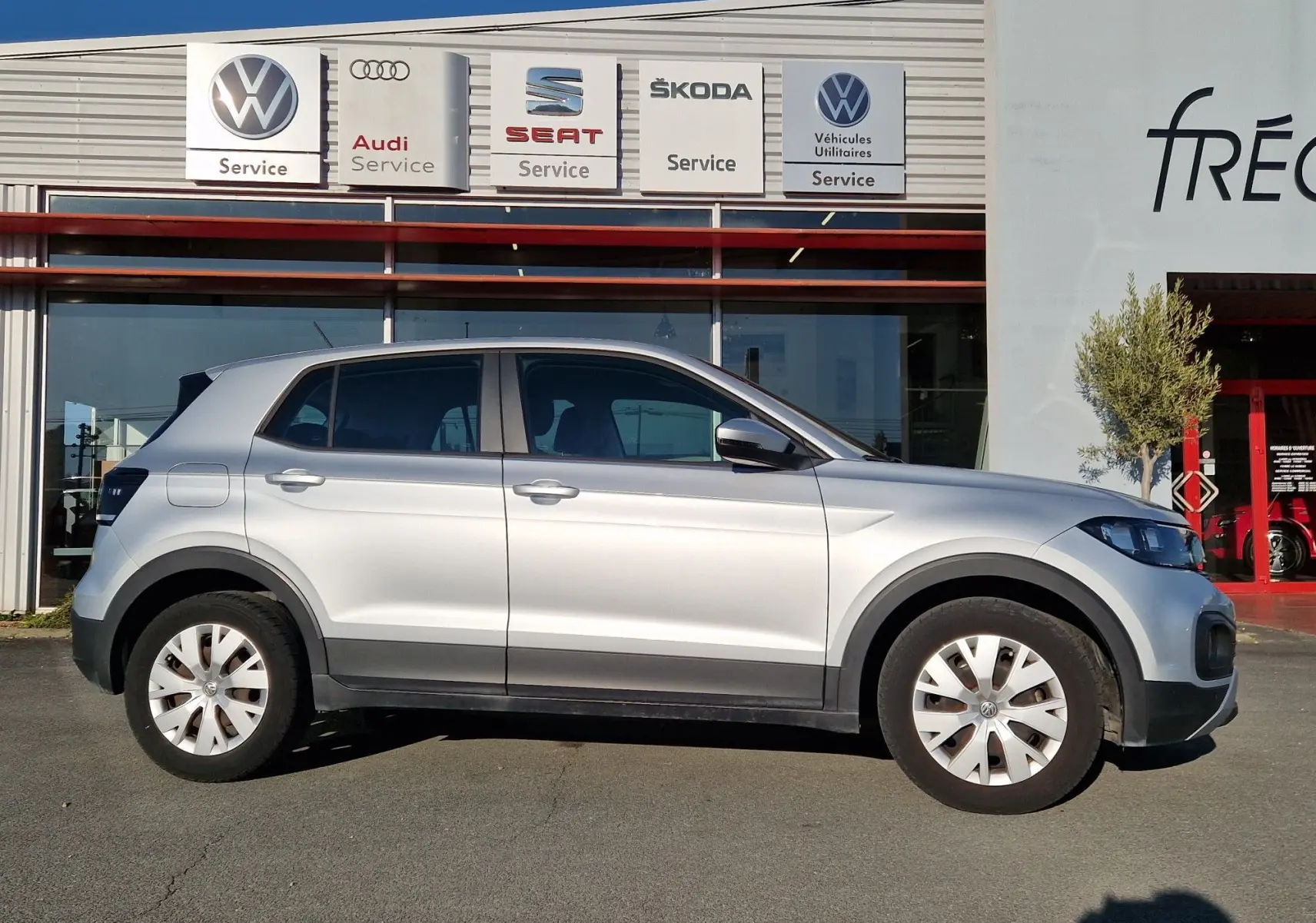 Profil côté gauche d'un Volkswagen T-Cross 1.0 TSI 95 Lounge argent métal, compact et moderne, sur fond de concession.