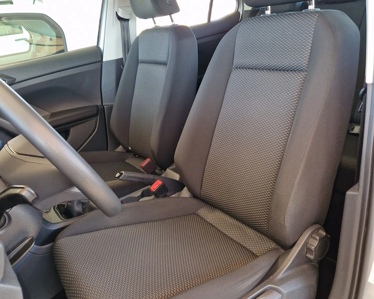 Vue intérieure côté conducteur du Volkswagen T-Cross 2019, sièges tissu gris foncé avec accoudoir central visible.