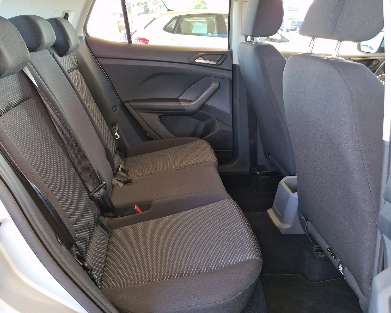 Vue intérieure arrière côté gauche du Volkswagen T-Cross argent métal 2019 avec sièges tissu gris et accoudoir central.
