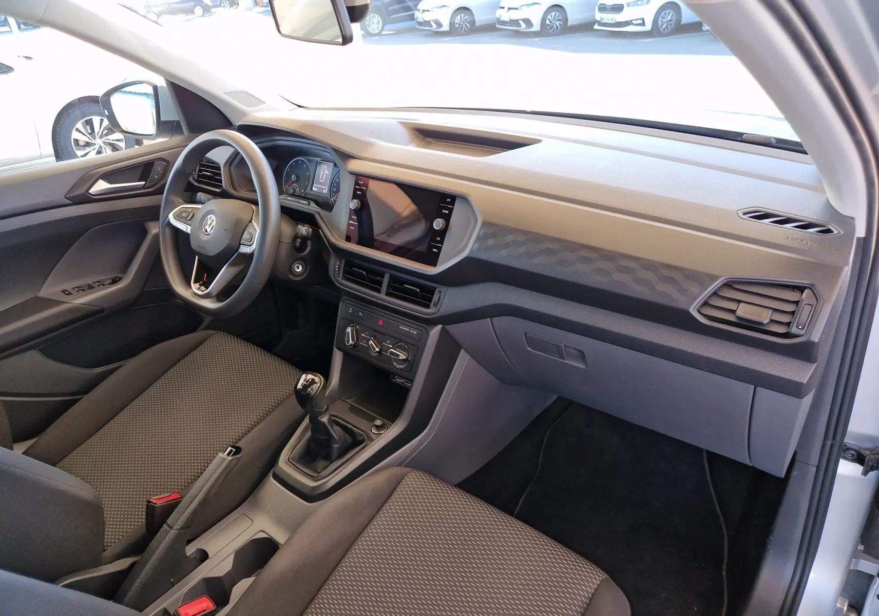 Vue intérieure côté conducteur du Volkswagen T-Cross 2019 argent métal, avec tableau de bord moderne et boîte manuelle.