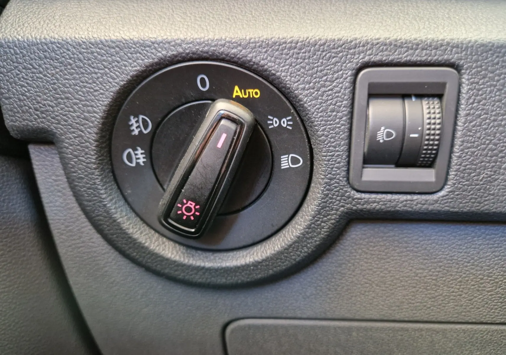 Gros plan sur le bouton de commande des phares du Volkswagen T-Cross argent métal, avec réglage automatique et molette d'intensité.