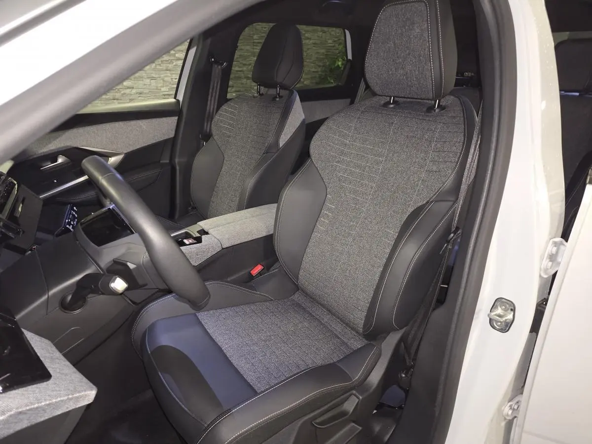 Vue intérieure côté conducteur du Peugeot 5008 blanc 2025, sièges tissu gris et cuir noir avec surpiqûres contrastées.