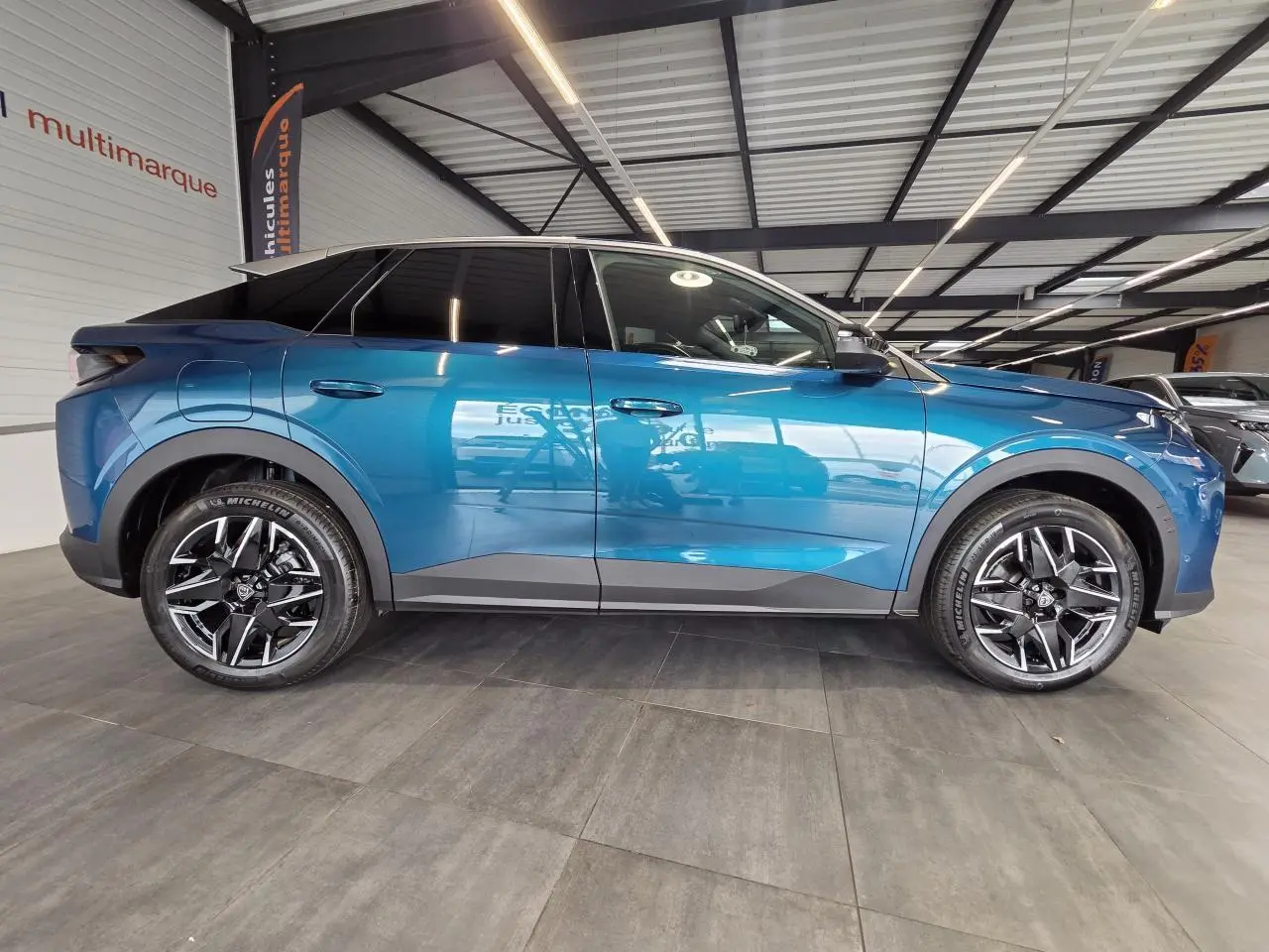 Profil droit du Peugeot 3008 hybride bleu métallisé avec jantes alliage 18 pouces et protections noires grainées.