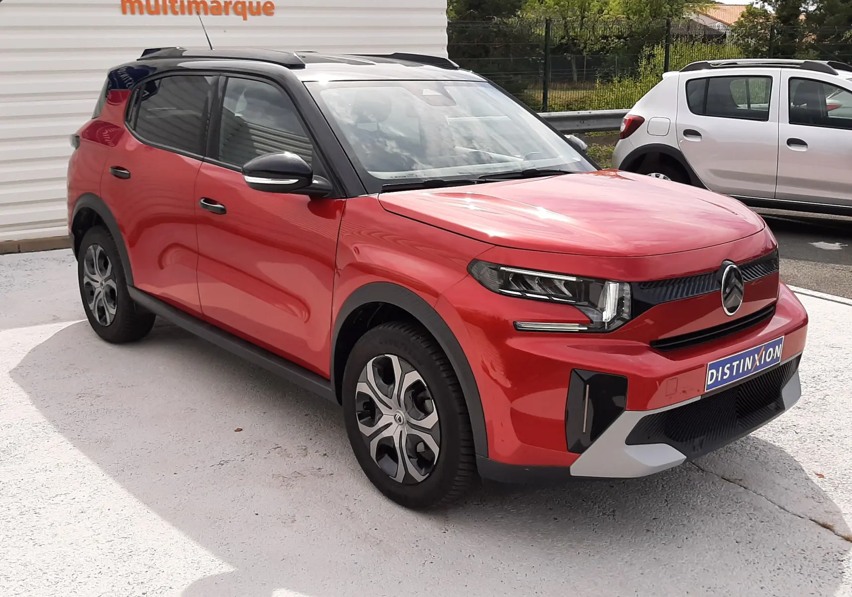 Vue 3/4 avant droite du Citroën C3 Aircross rouge Elixir avec toit noir, stationné devant un mur blanc.