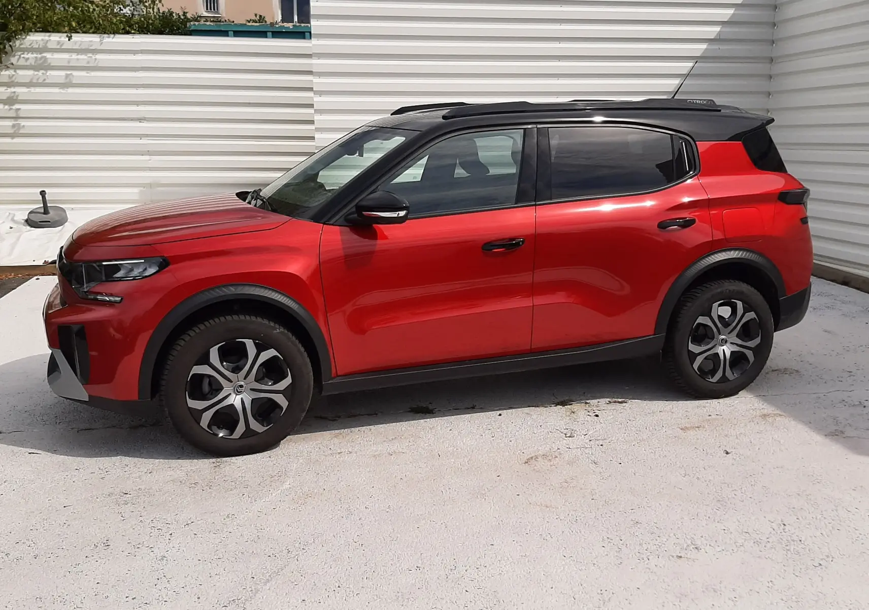 Citroën C3 Aircross rouge Elixir avec toit noir, vue de profil côté gauche sur fond clair et mur blanc.